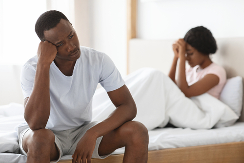 Upset young african american couple after fight in bedroom, sad man and woman sitting in bed apart
