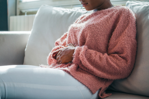 Woman in painful expression holding hands against belly suffering menstrual period pain, lying sad on home bed, having tummy cramp in female health concept