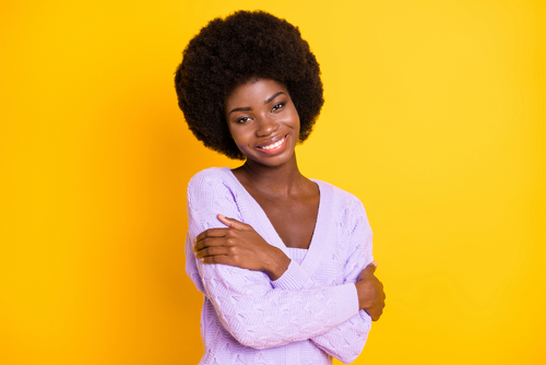 woman with afro against yellow background hugging self