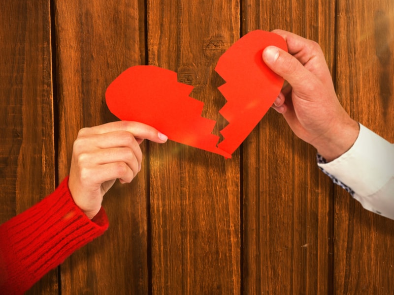A red paper heart being torn apart by two people 