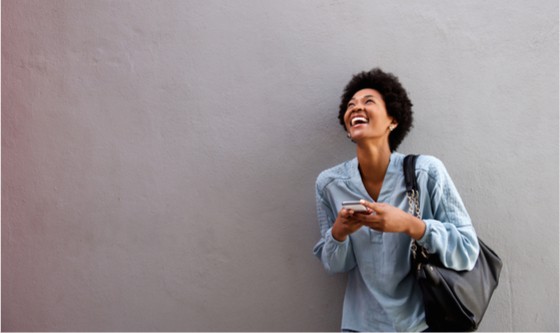 Happy woman on her phone in front of a grey wall 