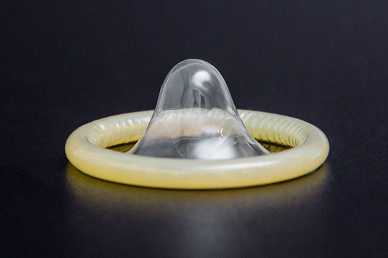 An unwrapped male condom placed in a dark surface