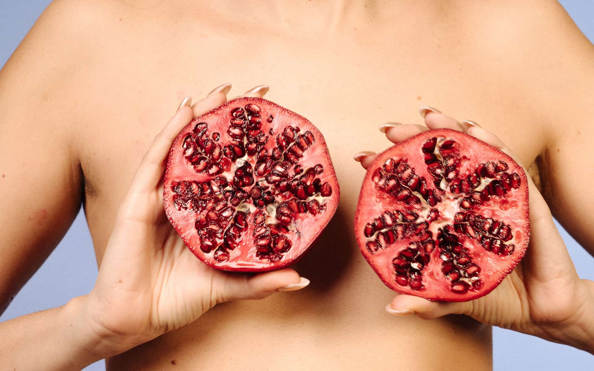 Woman holding up pomegranats in front of her torso, representing breasts