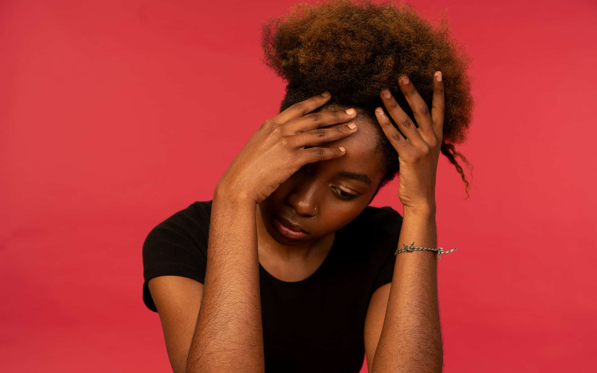 Young woman visibly upset, holding her head in her hands 