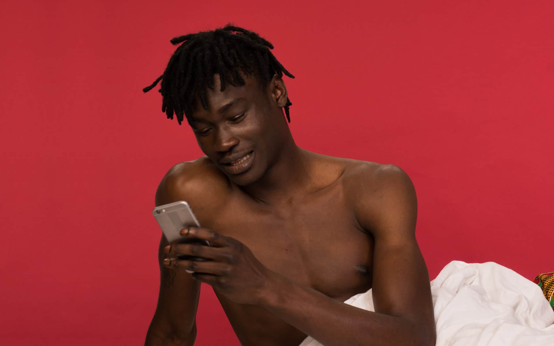 Man in bed alone, smiling at his phone 