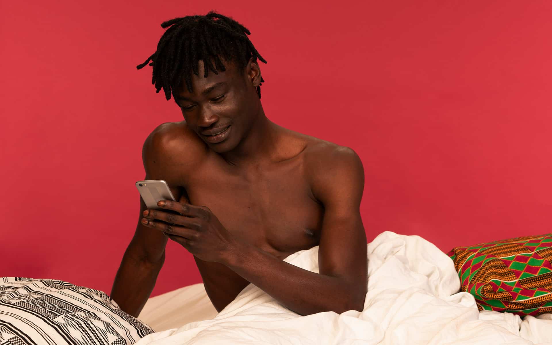 Man sitting in bed, smiling at his phone 