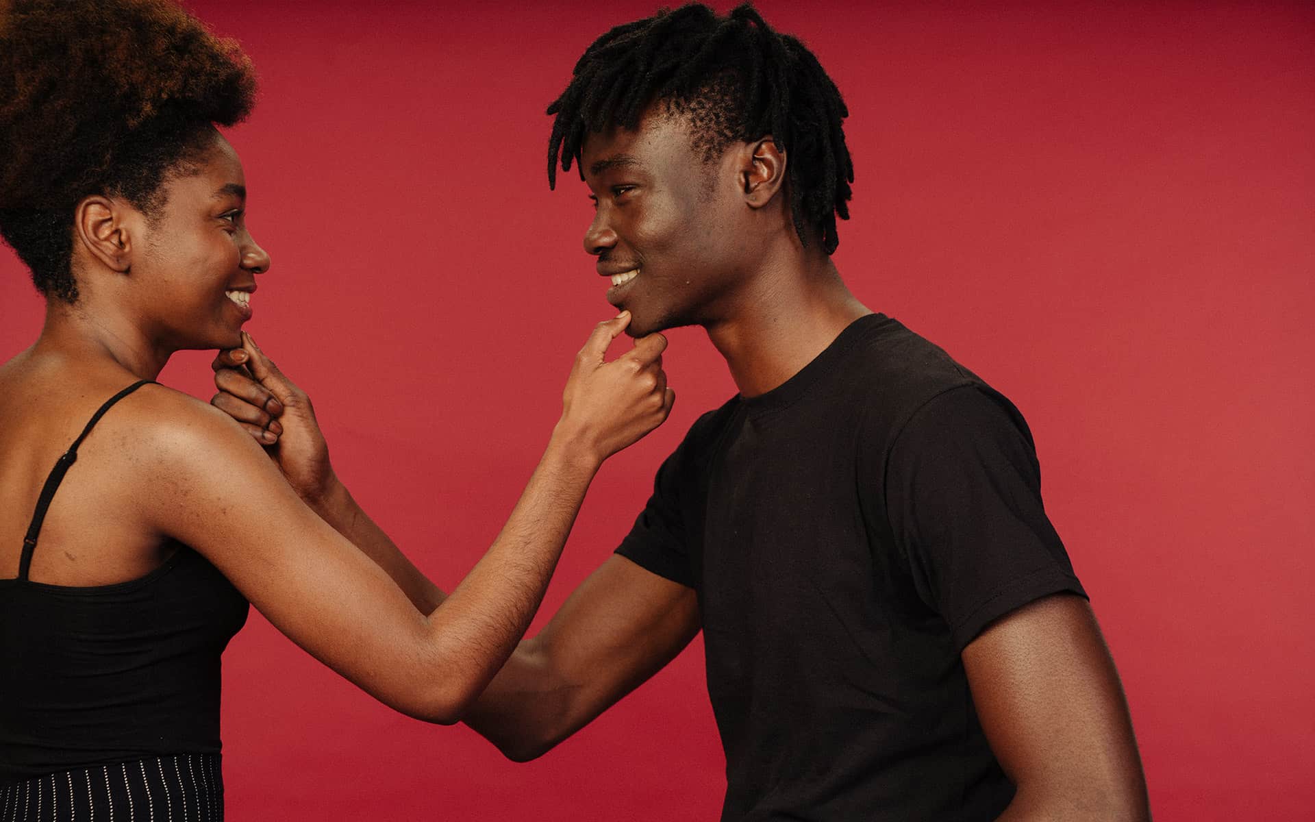 Two happy people dressed in black in front of red background 