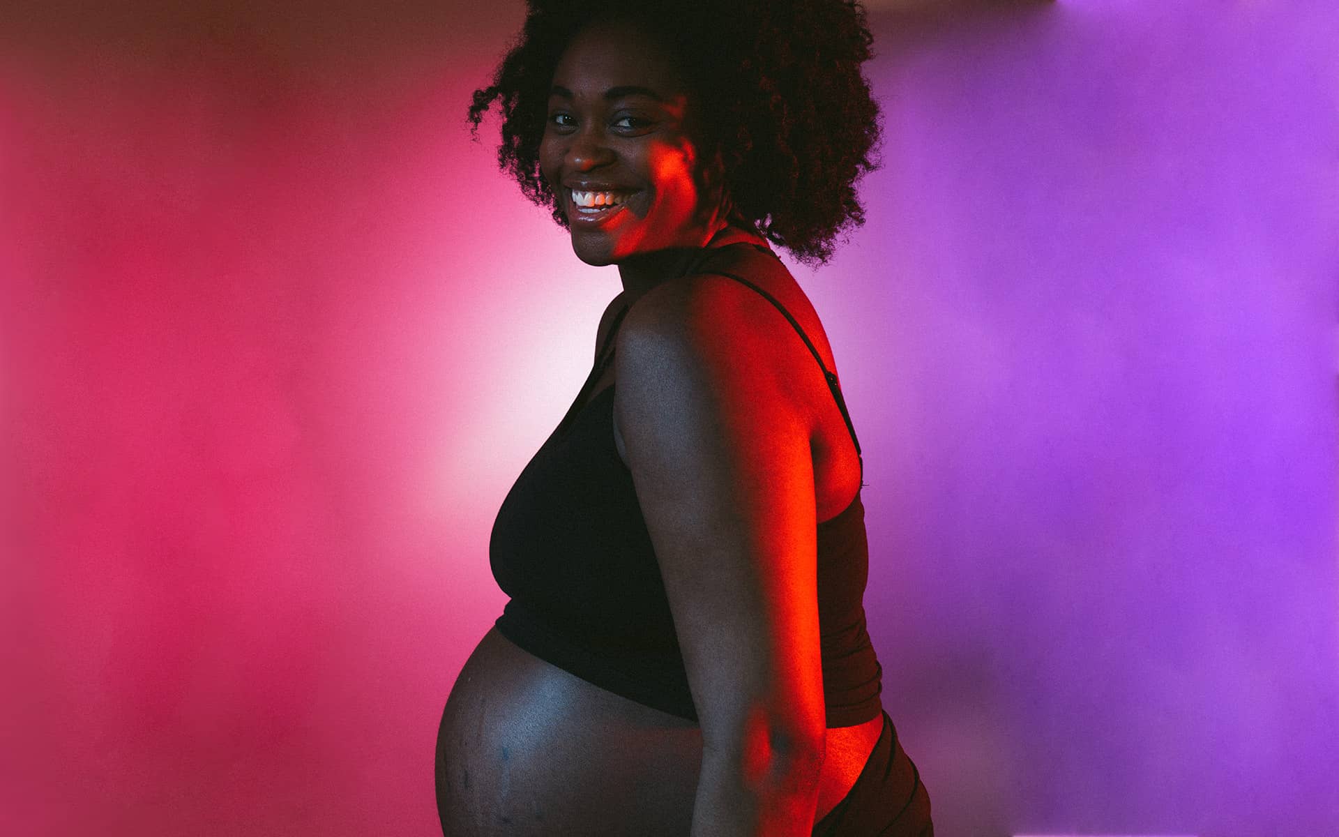 Heavily pregnant woman in front of a colourful backdrop