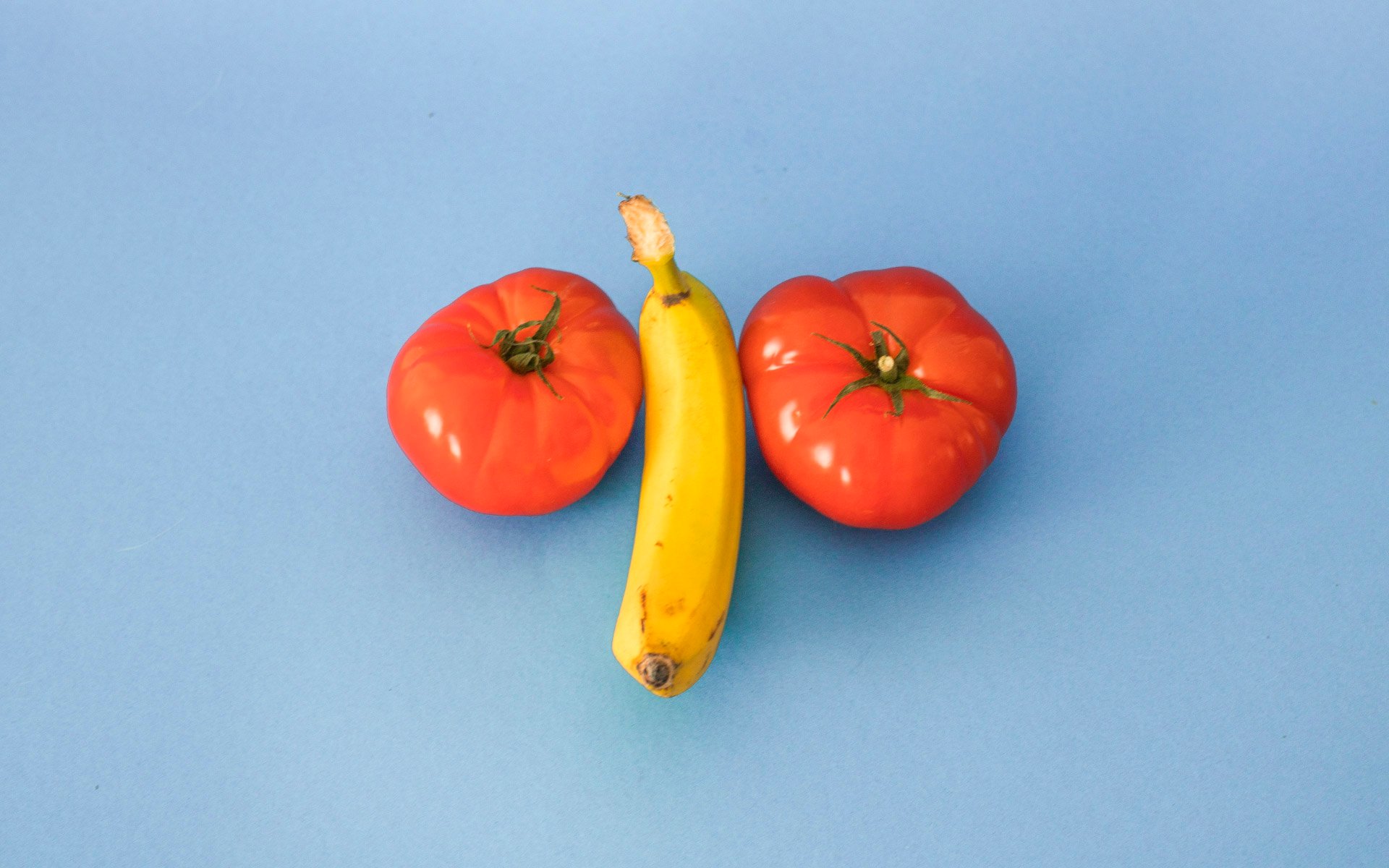 A yellow banana between two red tomatoes