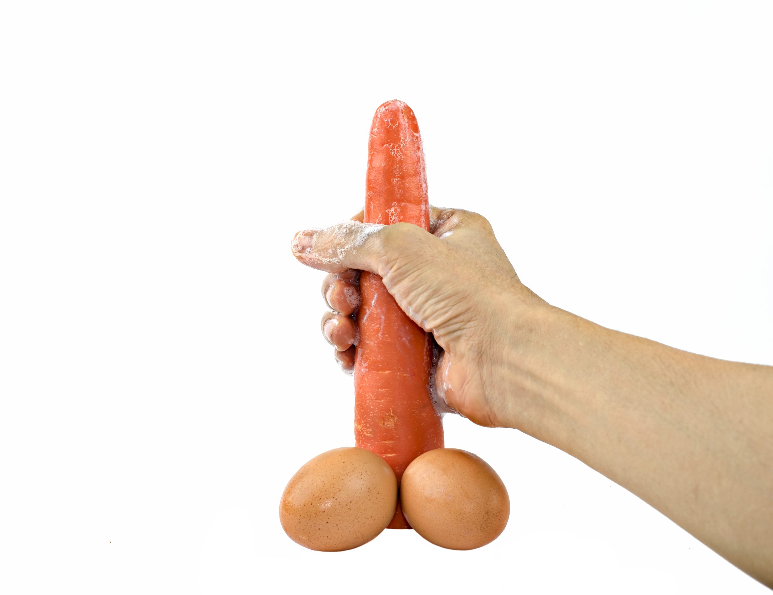 hand holding carrots and two eggs forming the shape of penis and balls respectively