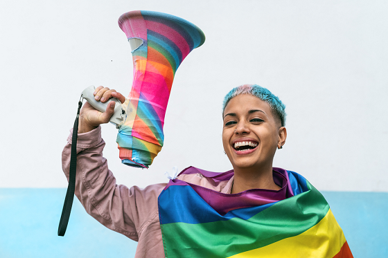 Man with colored hair and a colored flag holding a colorful loudspeaker