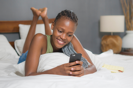 Woman laying in bed on her stomach scrolling through her phone