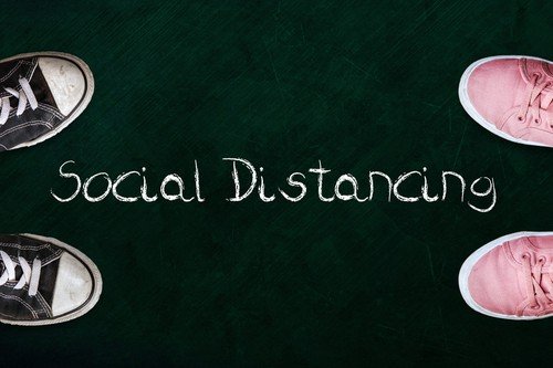 Two people standing on chalkboard with the word social distancing in between
