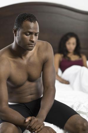 Tensed shirtless black man sitting on bed with blurred woman in background