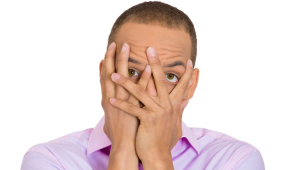  Closeup portrait, embarrassed young man covering face with hands with just enough space to peek through