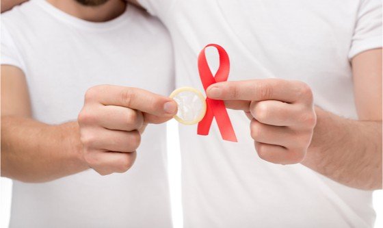 Two men embracing, holding up a condom and an AIDS ribbon 