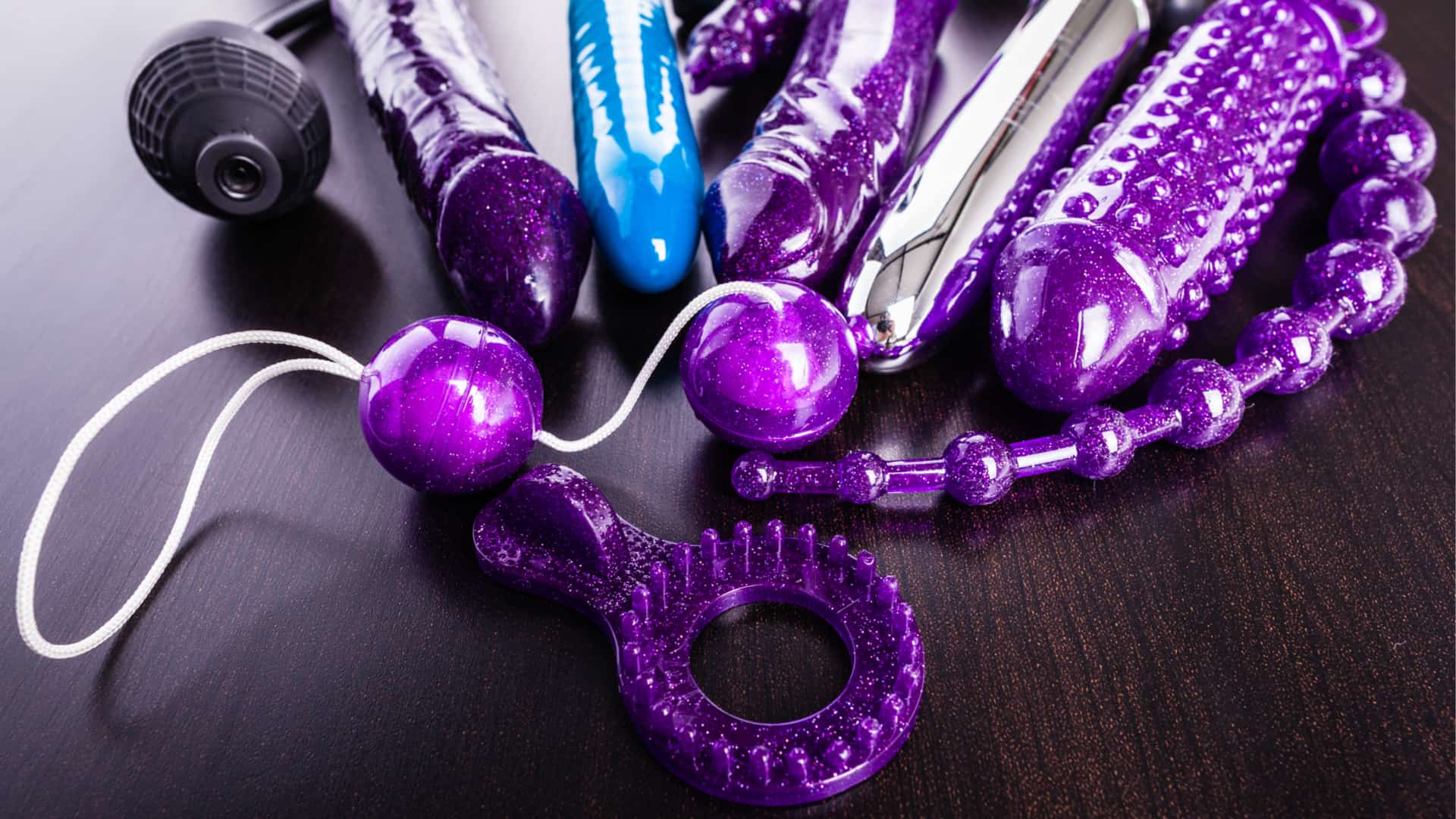 a collection of different types of sextoys, including dildo, vibrators and butt plugs over a dark wooden surface