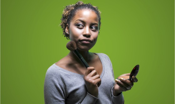 Young woman with make-up brush looking quizzical 