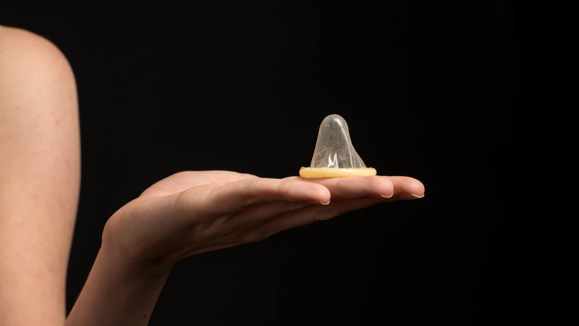 woman holding a condom on a black background. 