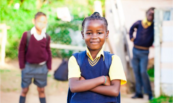 young african girl standing proud in her yellow and blue school uniform with siblings watching over her