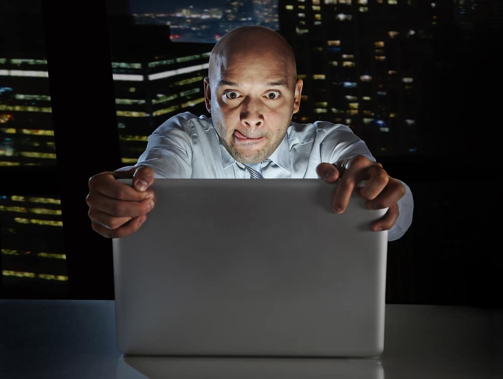 addict businessman alone at night sitting at office computer laptop watching porn or online gambling isolated on black background on internet chat addiction concept