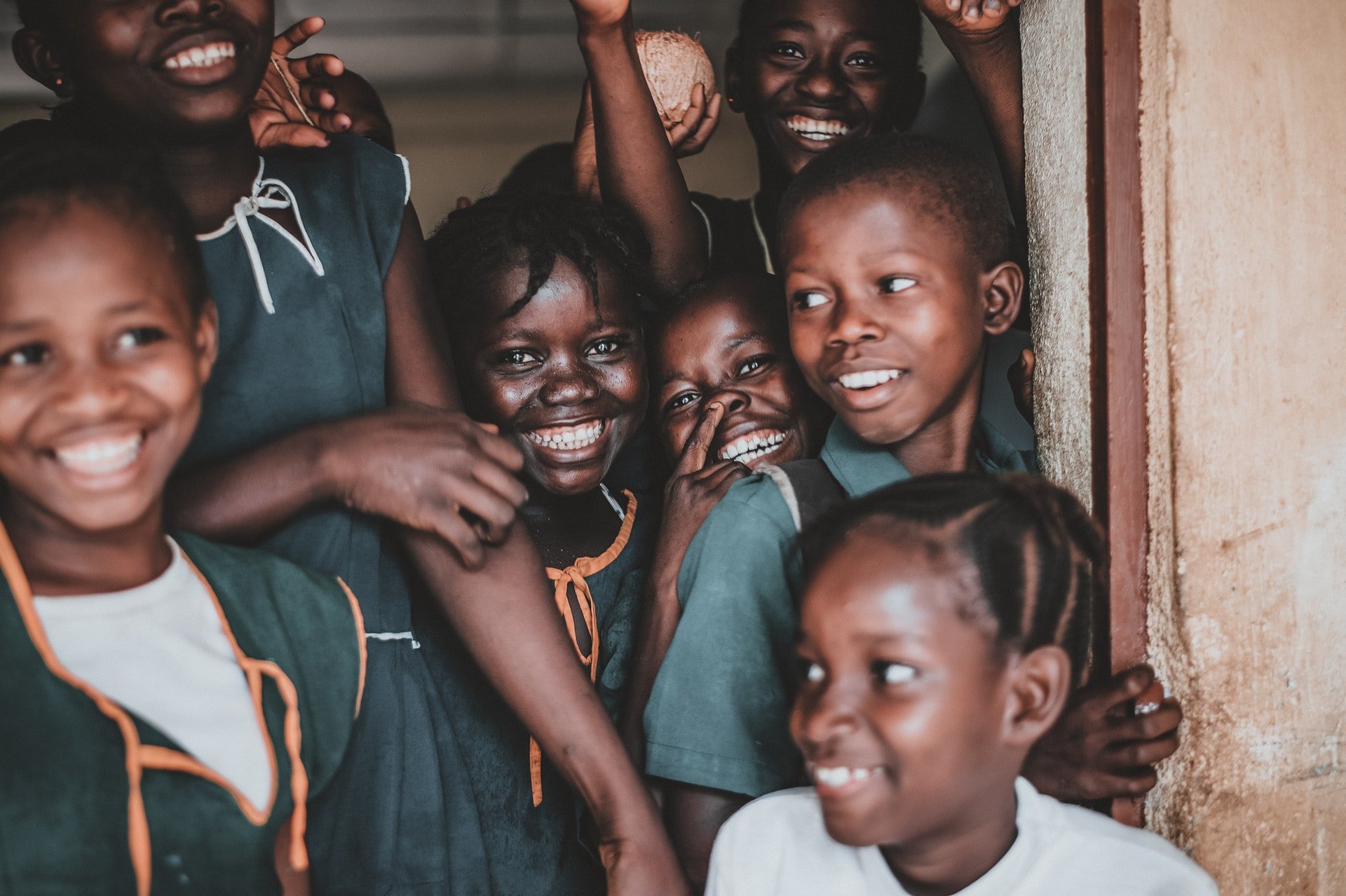 A group of young black girls in school uniform outside a classroom door, smiling