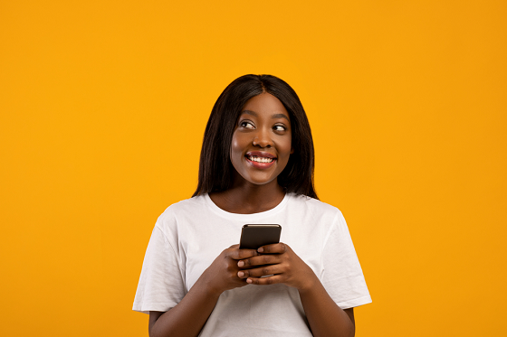 Woman standing against a mustard background holding phone 