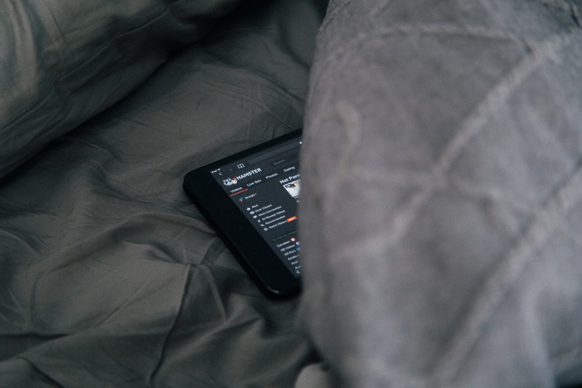 A tablet with a website open peeking out from underneath bedcovers