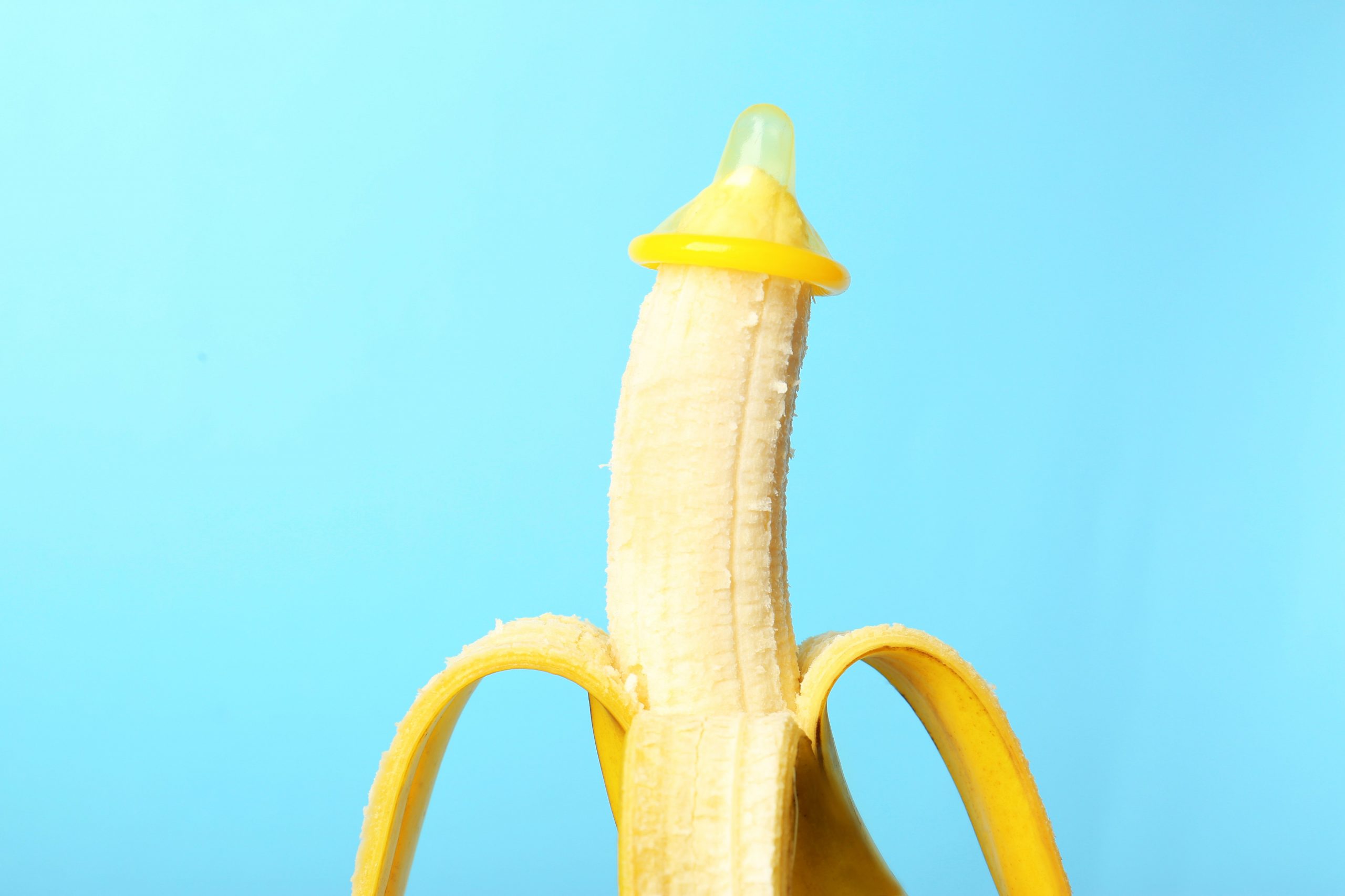 Condom on banana against sky blue background