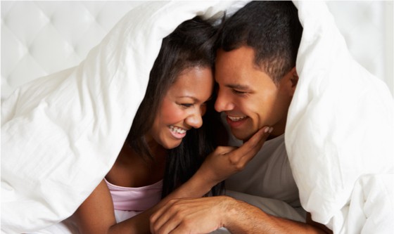 Happy couple cuddling underneath a blanket 