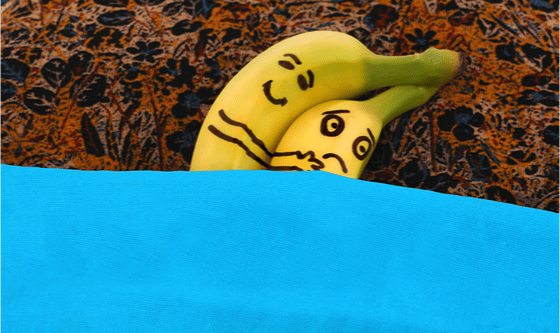 Two bananas in bed, cuddling, one is upset, the other is happy