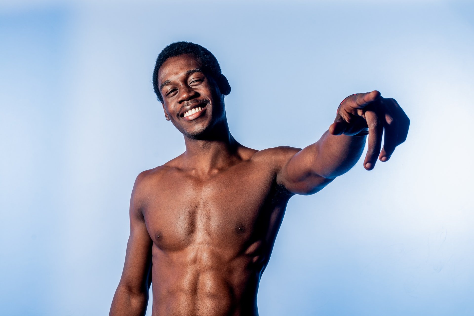 A topless young black man pointing into the distance