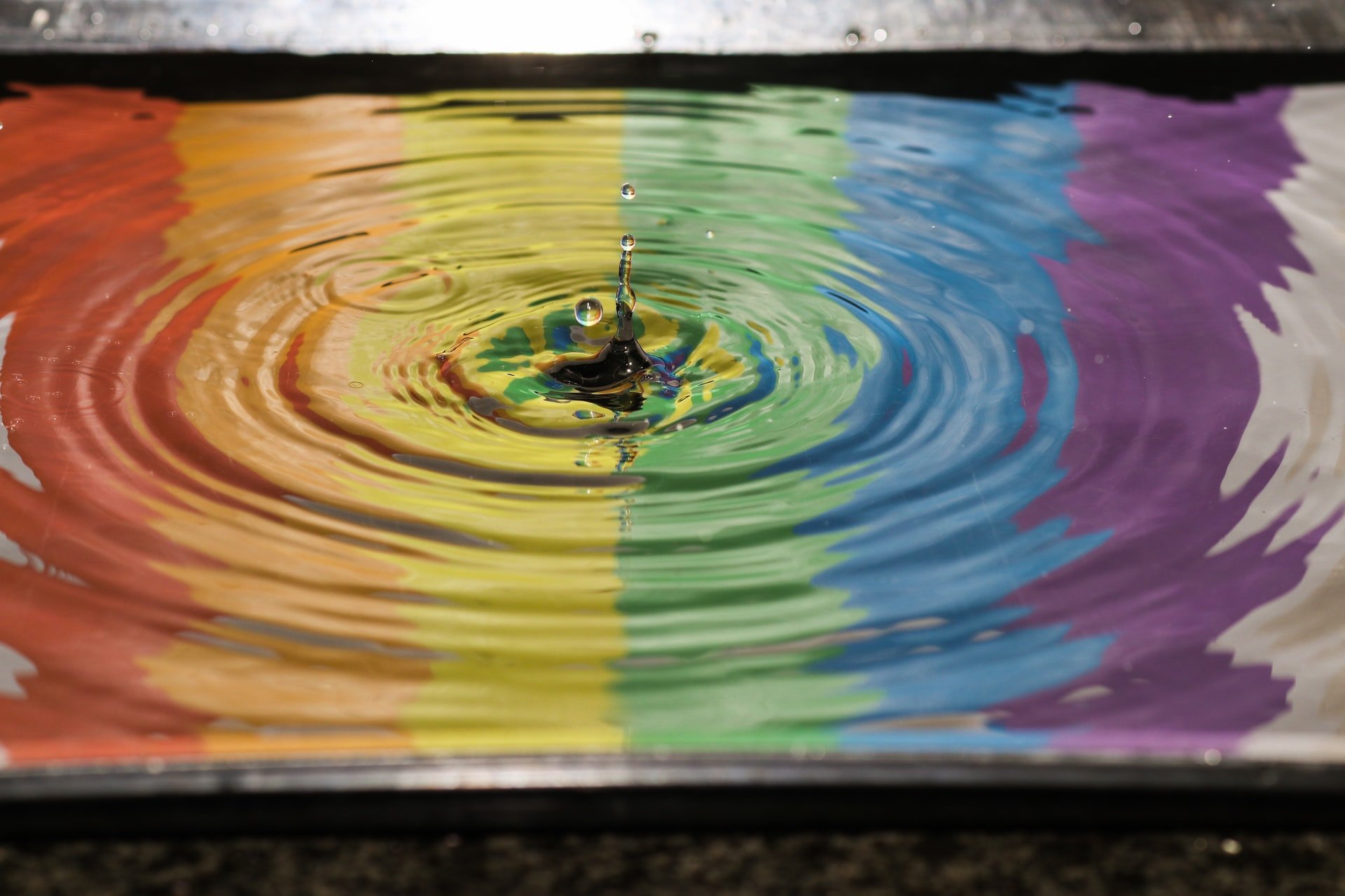 A picture of a drop landing in a raindbow coloured pool and distorting the surface