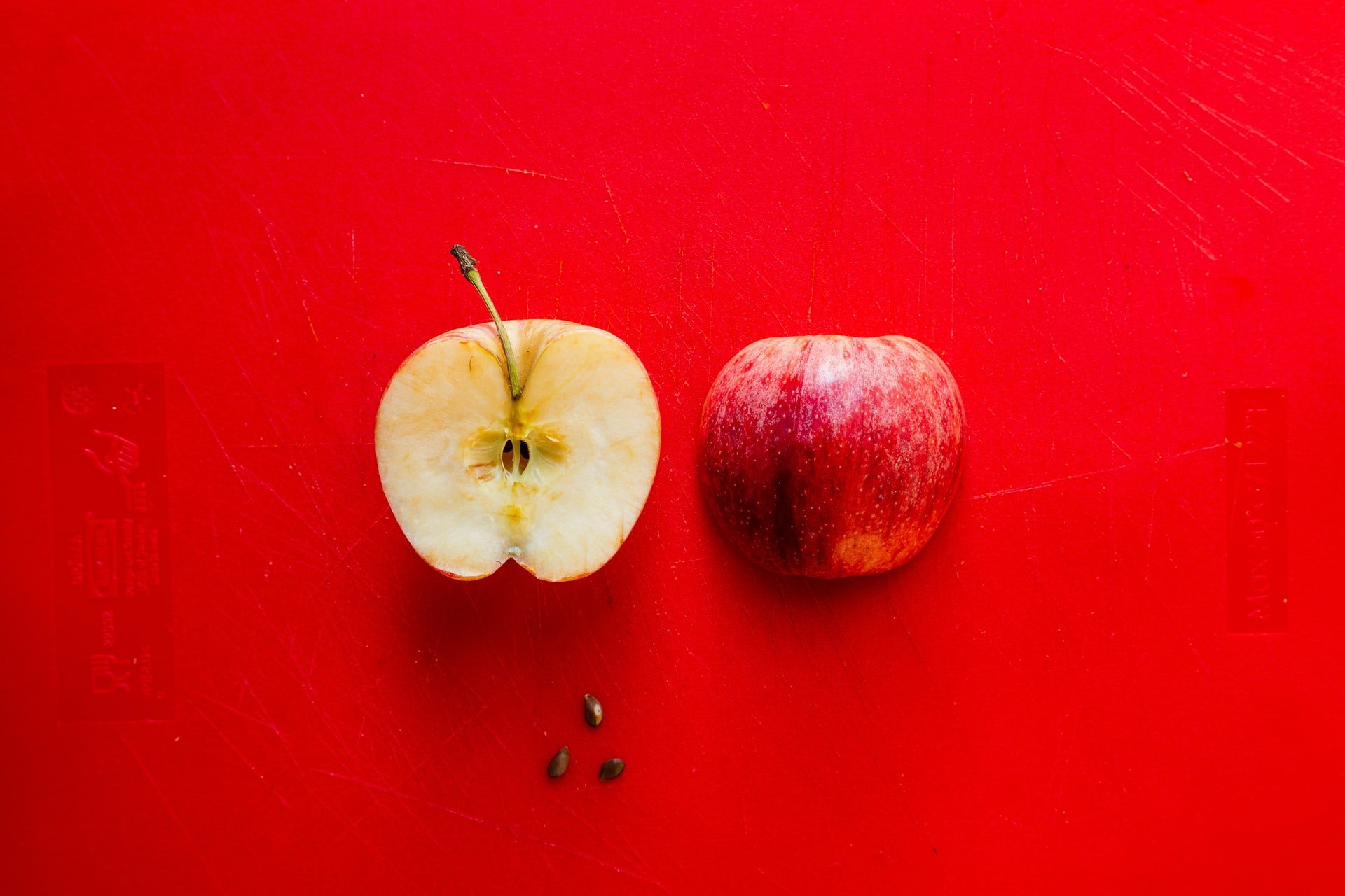 A split red apple with a few of its seeds scattered around it
