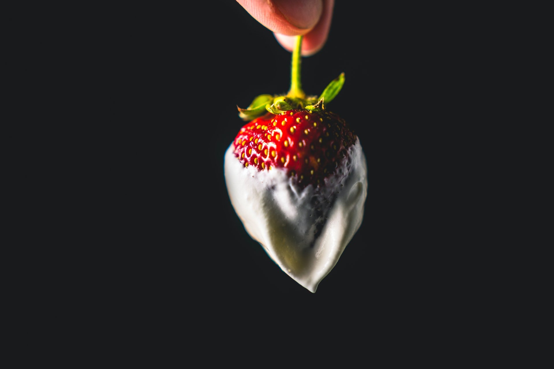 A hand holding a strawberry dipped in cream