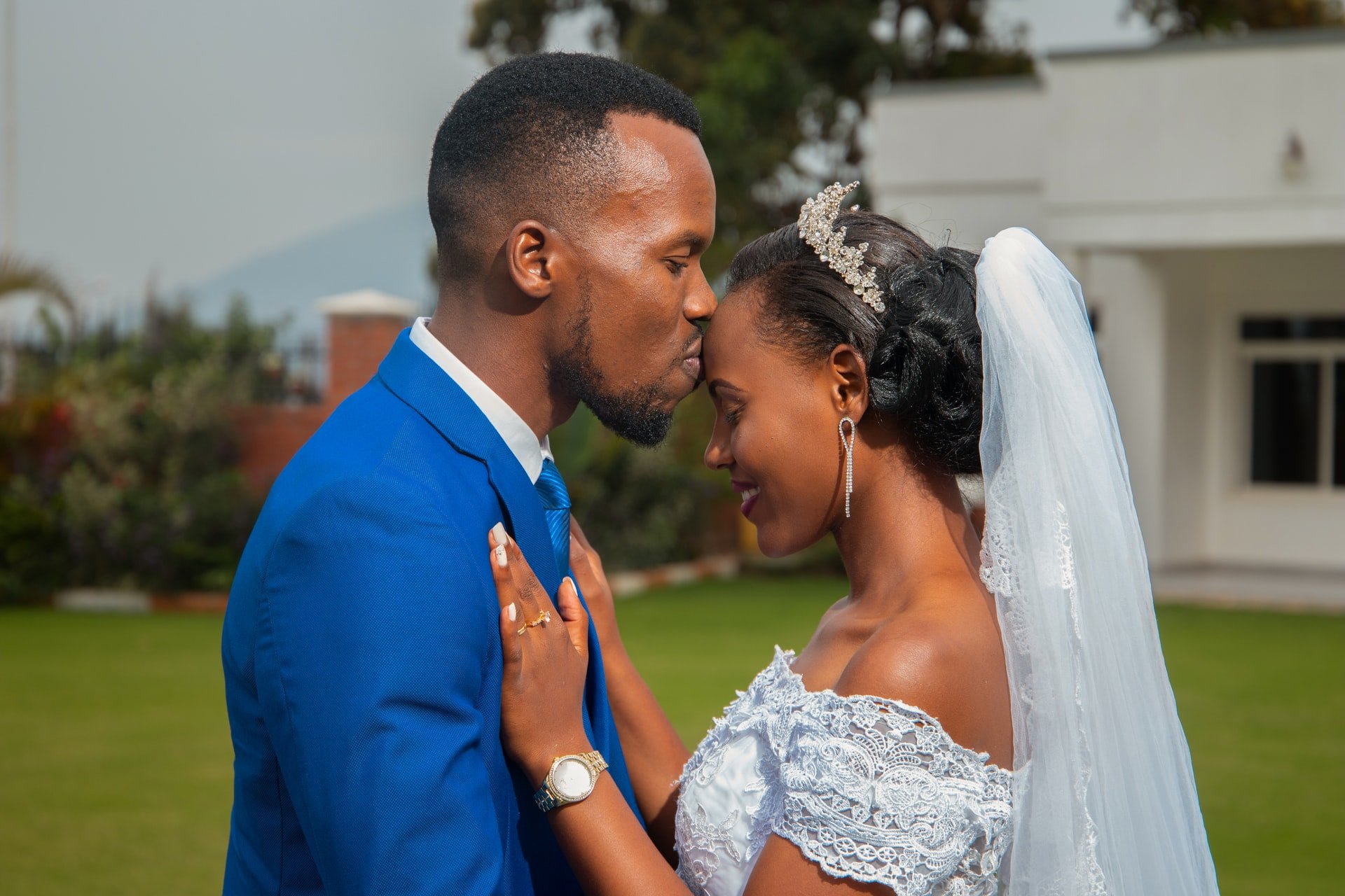 A black couple on their wedding day; the man is kissing the woman's forehead
