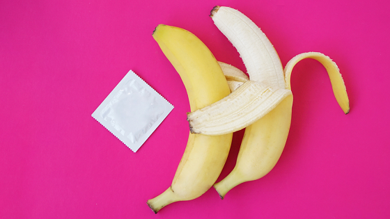 Two bananas, one peeled near a pack of condom