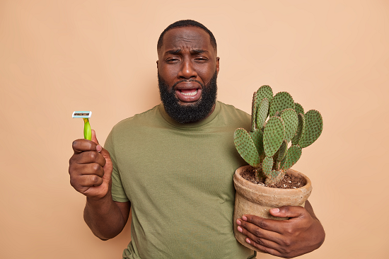 sad man holding shaver and cactus plant in a pot