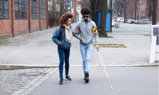 A black girl helping a blind man cross the road