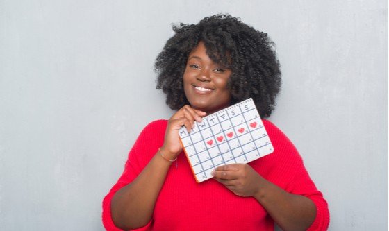 A black woman holding up a calendar with a period cycle marked on it