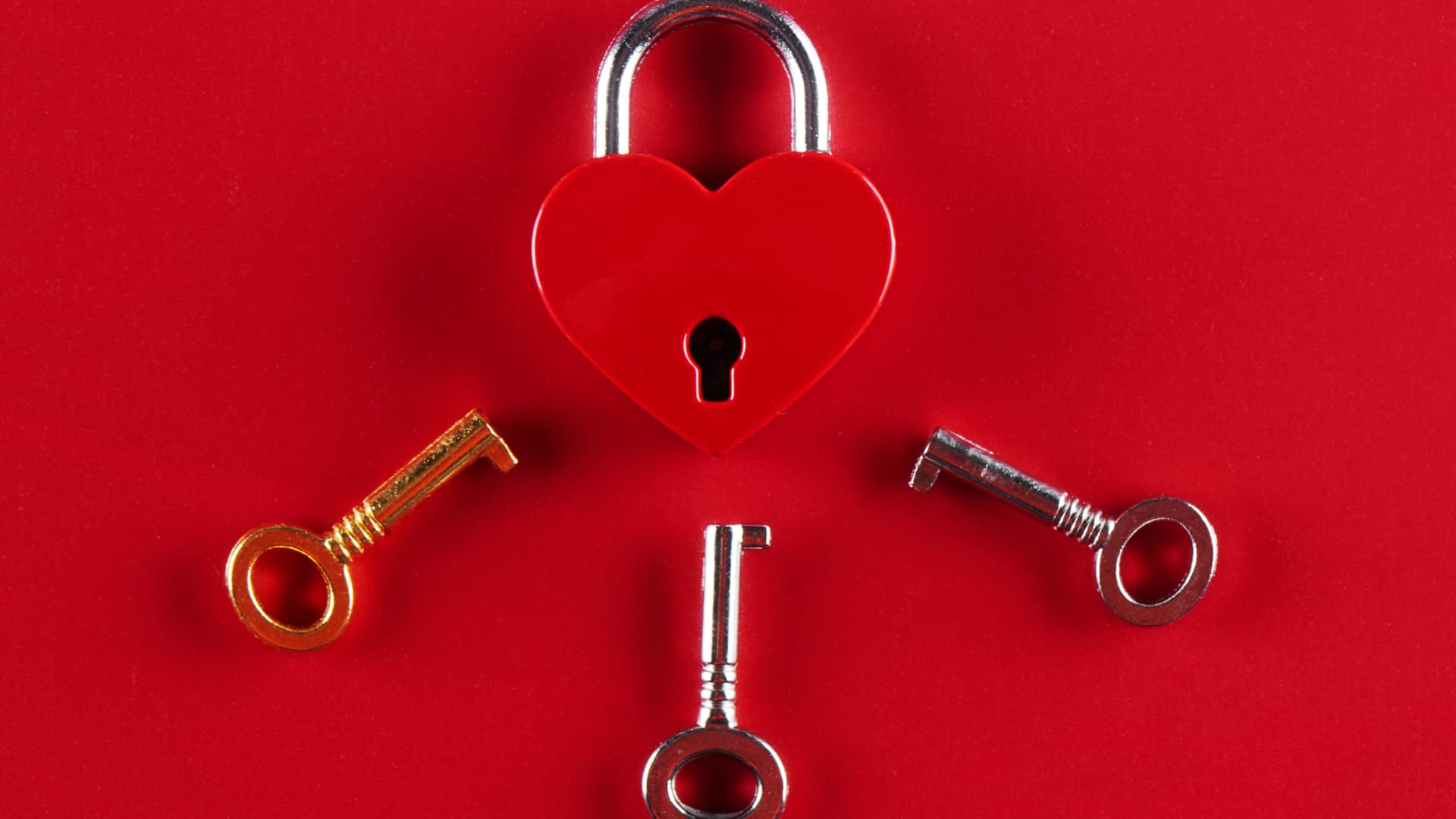  A heart shaped lock and three keys to it on a red background
