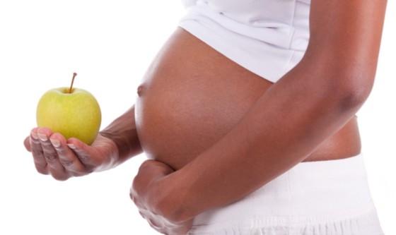 An image of a pregnant woman's belly, her holding an apple 