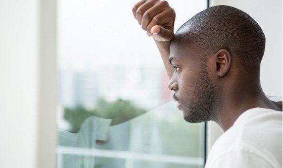 A young black man, looking out of a window, troubled