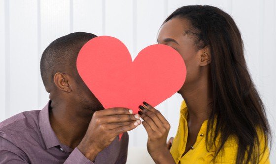 a black couple hiding behind a cutout of a big red heart