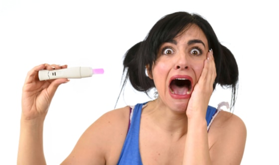 young pregnant woman scared in shock checking pink positive result on pregnancy test