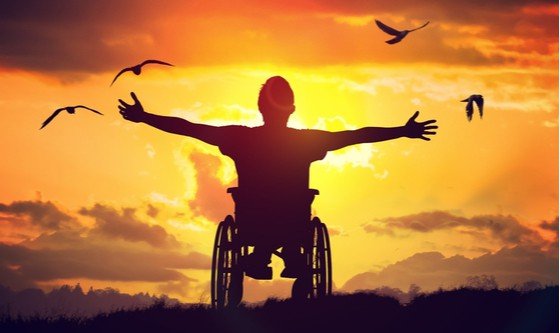 A disabled man on a wheelchair spreading his arms towards the sunset