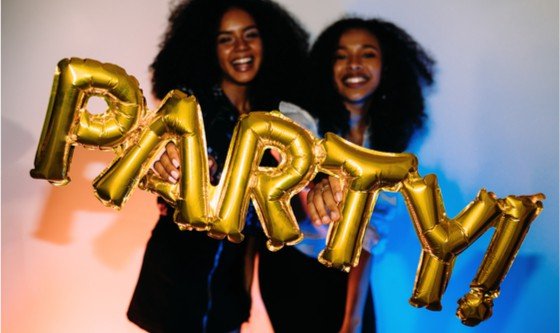 Two younbg women holding up a balloon spelling 'party' 