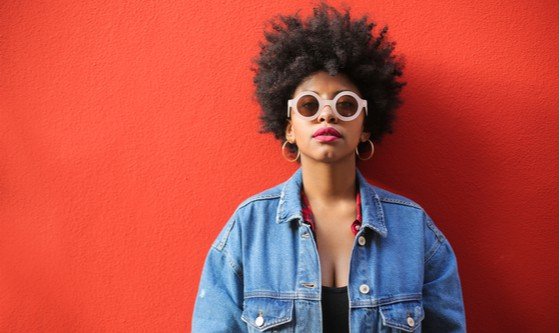 fashionable independent women with an afro, sunglasses and denim jacket on a red background