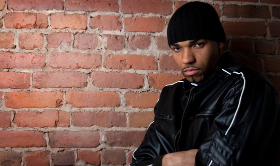 Dark and gloomy guy dressed in black, leaning against the brick wall.