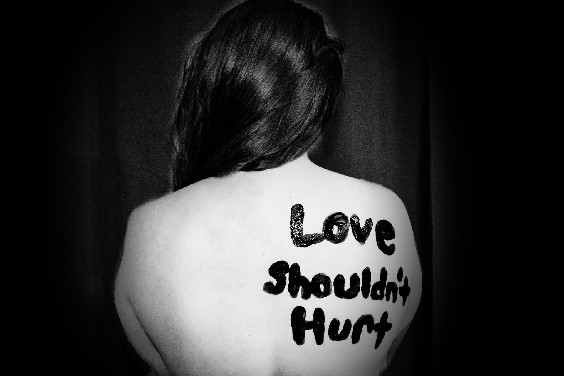 A girl with her back to the camera with the words 'Love Shouldn't Hurt' painted on